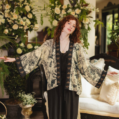 Woman in a floral kimono-style outfit standing in an elegant room with floral decorations.