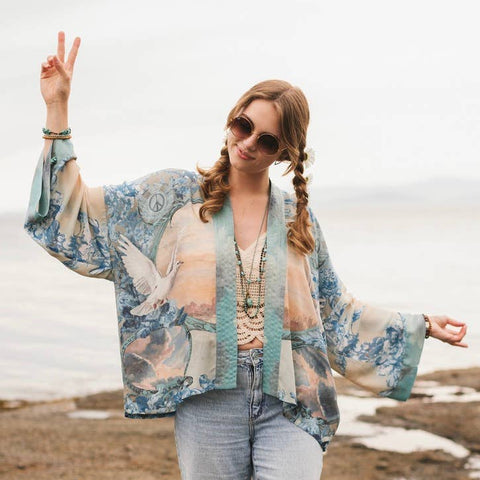 Woman wearing a floral kimono and sunglasses on a rocky beach.