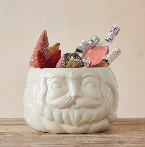 White ceramic mug with a face design filled with decorative bottles and plants on a wooden surface.