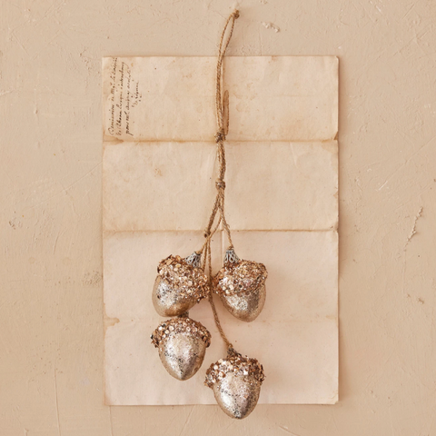 Decorative acorn ornaments hanging from twine on a textured beige background