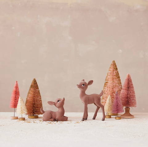 Two deer figurines standing among colorful bottlebrush trees on a neutral background