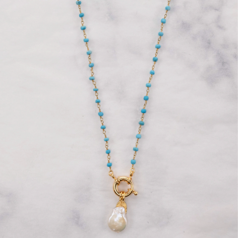 Necklace with turquoise beads and a pearl pendant on a marble background, branded 'Julio Designs'.