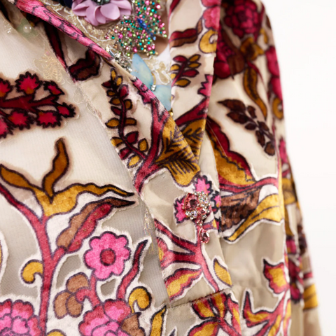 Close-up of a patterned fabric with floral and abstract designs in pink, blue, and brown on a beige background.