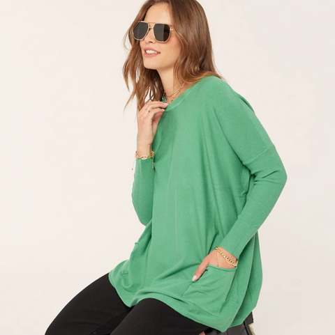 Woman wearing a green oversized sweater and black pants on a white background