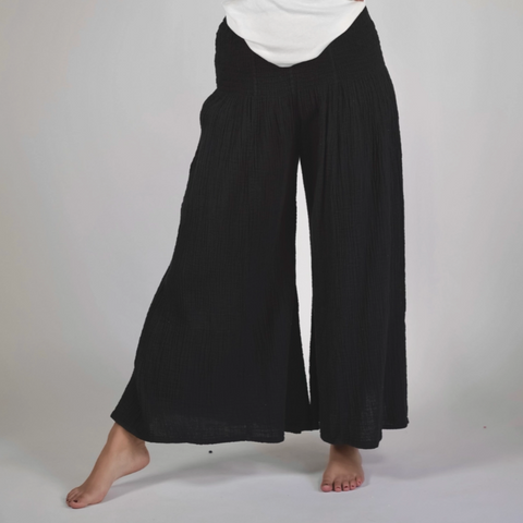 Woman wearing a white top and black wide-leg pants on a plain background