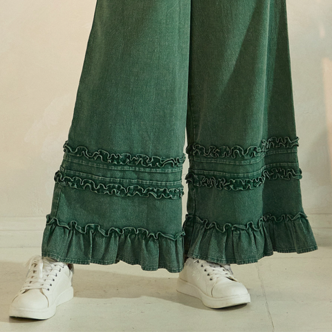 Green denim pants with ruffled cuffs worn with white sneakers on a neutral background