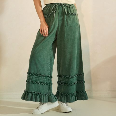 Woman wearing a cream top and green pants with ruffled hem against a plain background