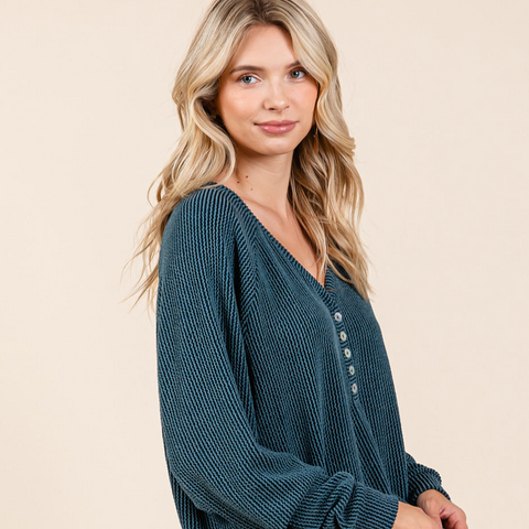 Woman wearing a teal ribbed sweater with buttons on a beige background