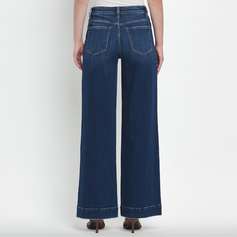 Person wearing blue wide-leg jeans and a white top on a plain background