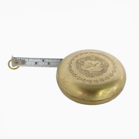 Brass tape measure with decorative lid on a white background
