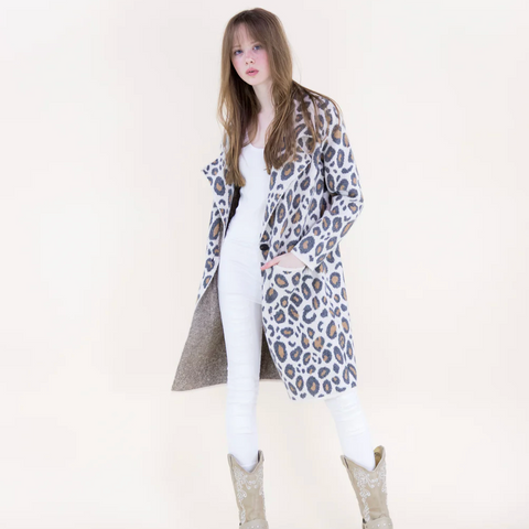Woman wearing a leopard print coat over a white outfit with beige boots on a white background