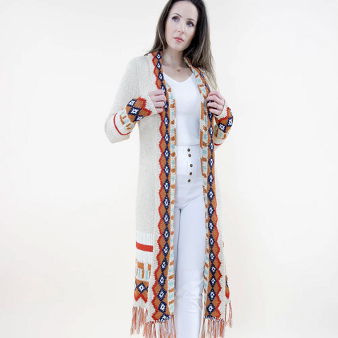 Woman wearing a long, patterned cardigan with fringes on a white background