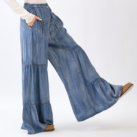 Person wearing a white long-sleeve top and blue denim wide-leg pants on a white background