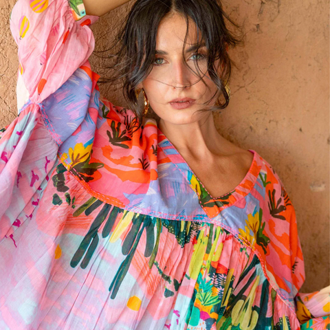 Woman wearing a colorful floral dress against a textured wall.